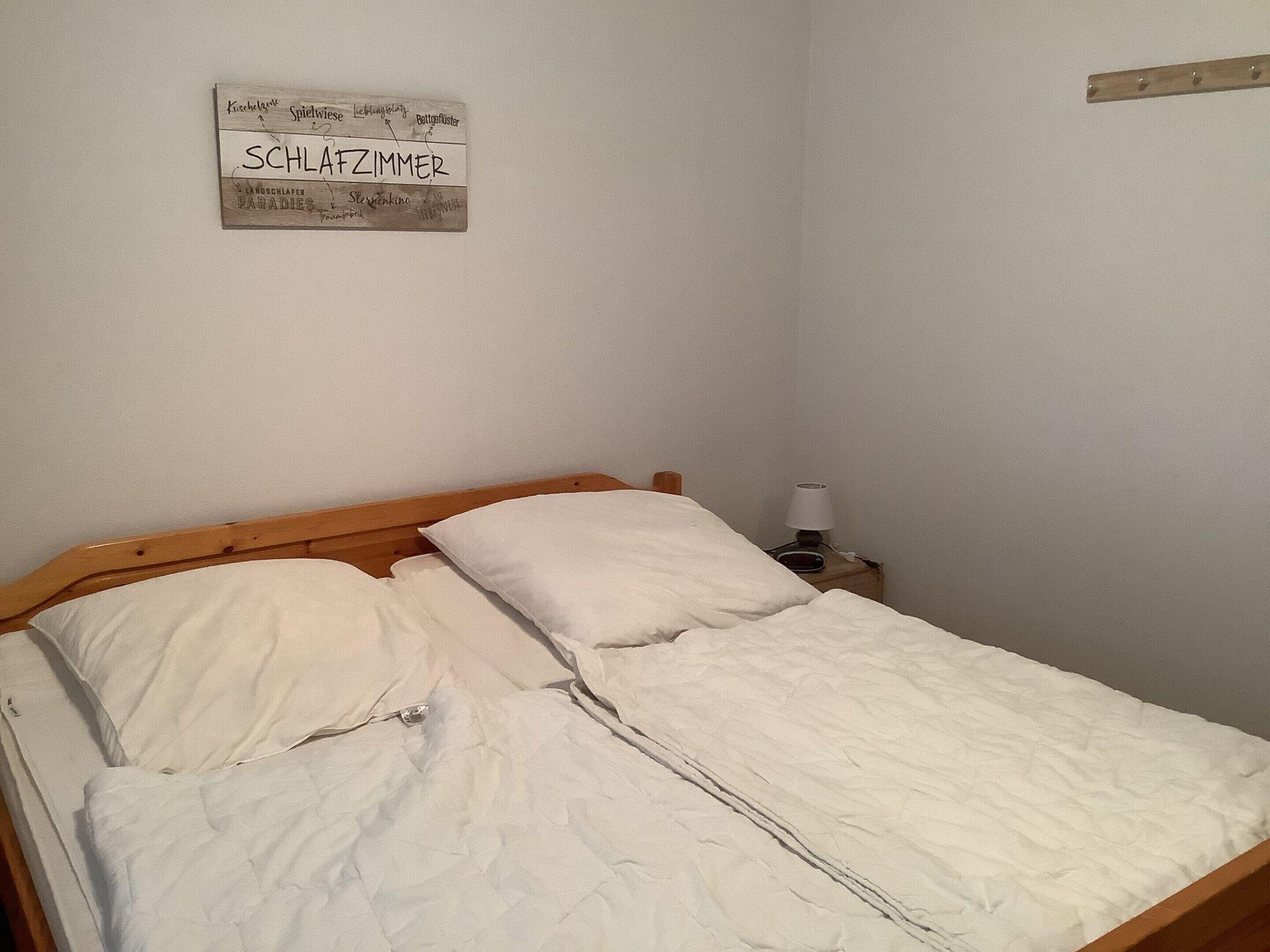 Ein schlichter, schlichter Schlafzimmer mit einem Holzbettgestell, weißer Bettwäsche und einem Schild an der Wand.