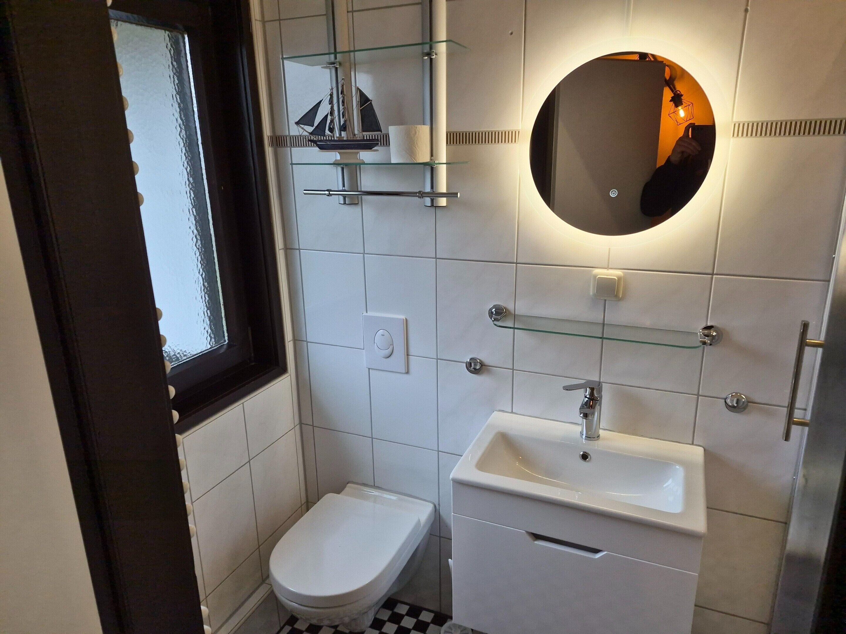 A modern bathroom with a toilet, sink, and a small ship decoration on a shelf.