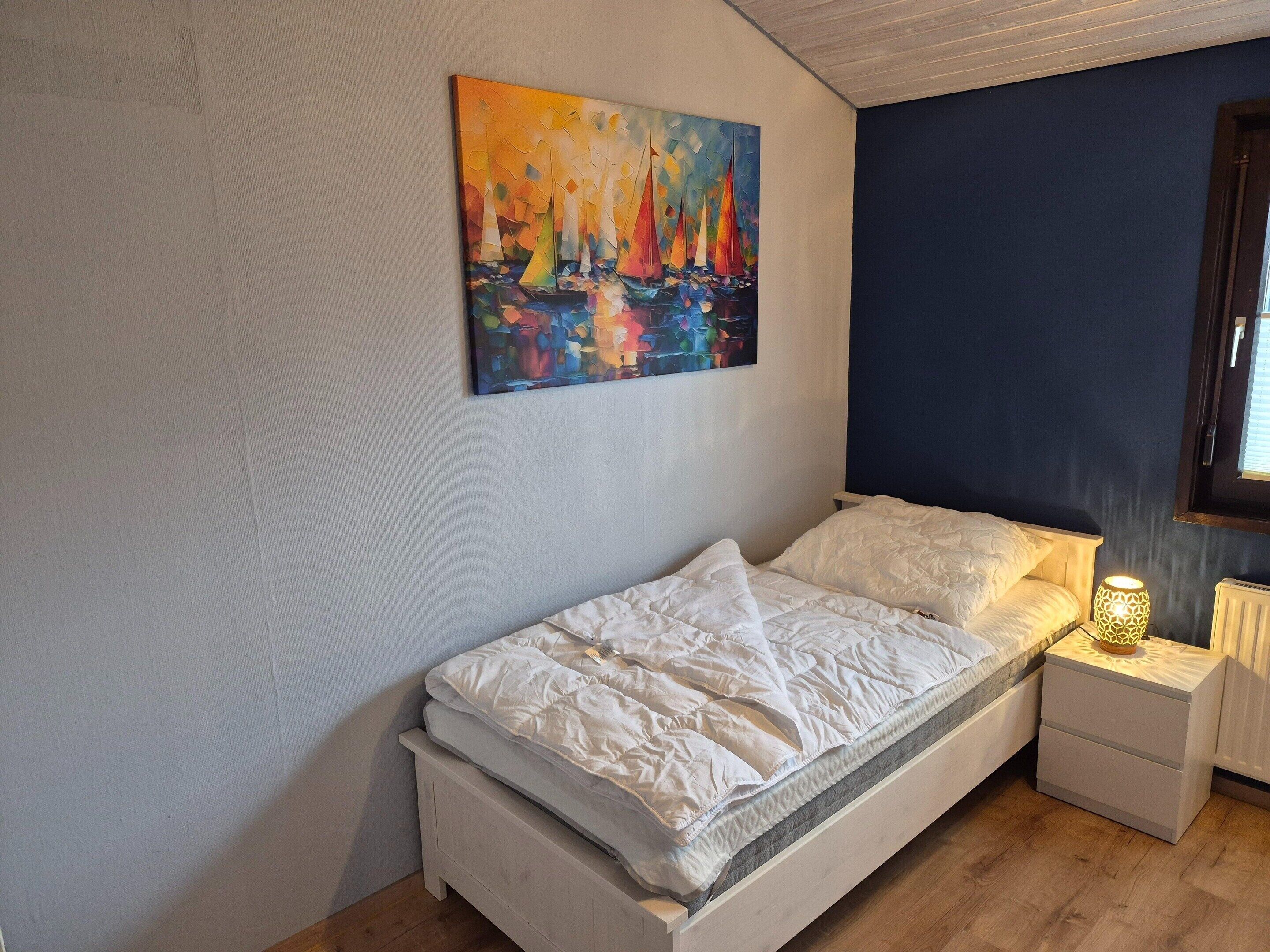 A bedroom with a bed, a nightstand, a lamp, and a painting on the wall.