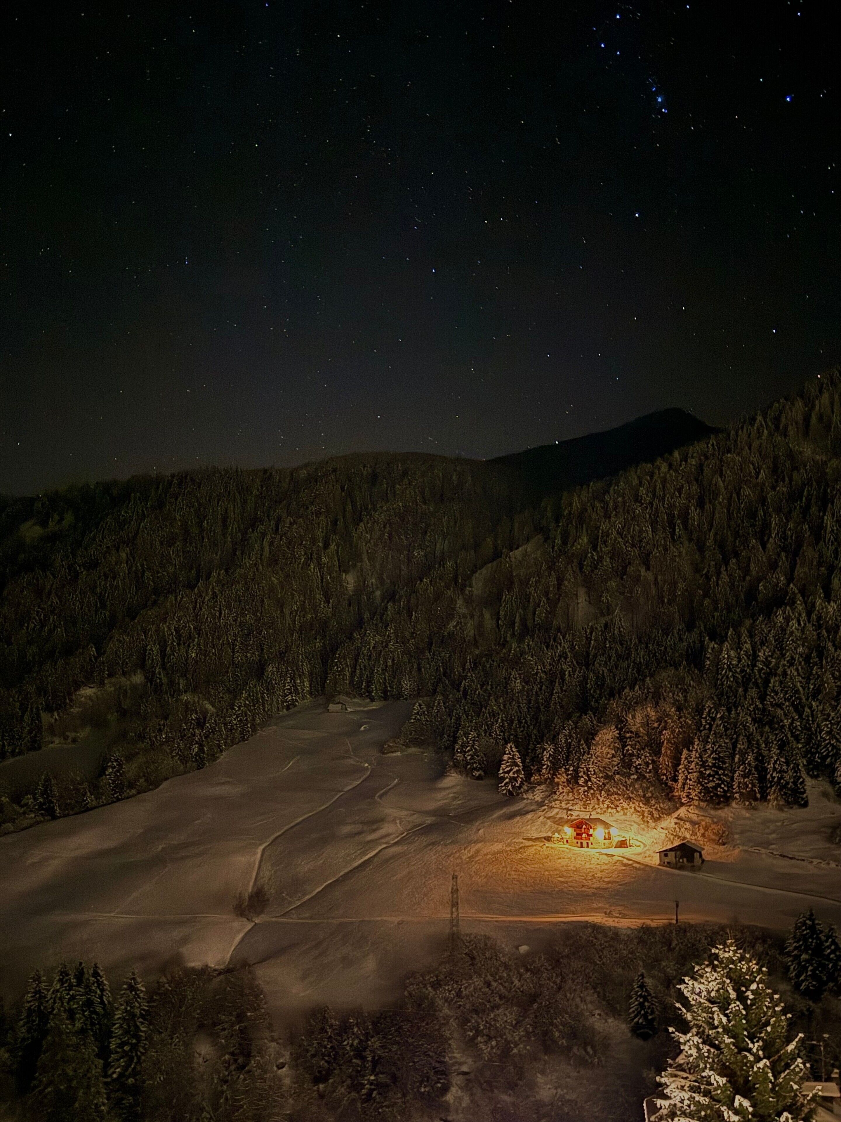 A snowy landscape with a cabin and a forested hill.