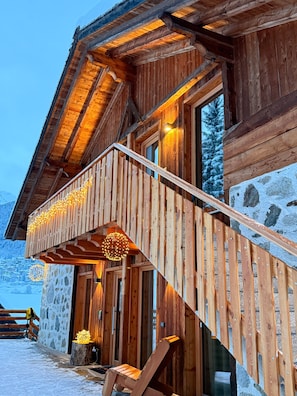 A wooden cabin with a balcony, stone walls, and a wooden staircase.
