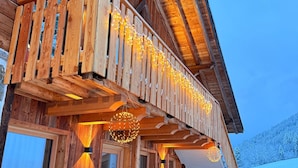 Una baita in legno con un balcone, gradini in pietra e una panchina.