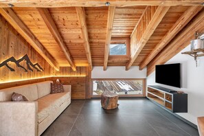 Un interior moderno con techo de madera, un televisor grande, un sofá y vistas por una ventana.