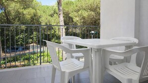 A balcony with white plastic chairs and a table, overlooking a road and greenery. - Cozy apartment near the beach in Rosolina (Rosolina Mare)
