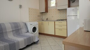 A compact kitchen with a washing machine, a sofa, and a refrigerator. - Cozy apartment near the beach in Rosolina (Rosolina Mare)