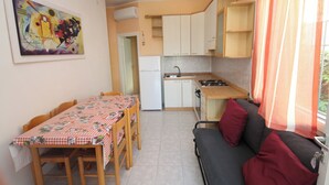 Ett kompakt kök med ett matbord och stolar, en soffa med kuddar och en tavla på väggen.