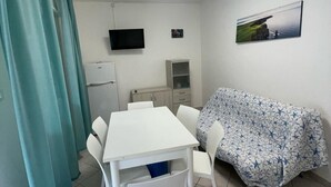 Ein gemütlicher Wohnbereich mit Esstisch, weißen Stühlen, einer Couch mit Blumenmuster, einem Flachbildfernseher und einem kleinen Kühlschrank.