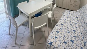Ein Zimmer mit einem weißen Tisch, weißen Stühlen, einem Bett mit Sternenmuster, einem Fernseher, einem Kleiderschrank und einem Fenster mit Vorhängen.
