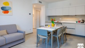 A modern kitchen with white cabinets, a dining table with chairs, and a grey sofa. - WANT OF LAKE by Design Studio (Colico)
