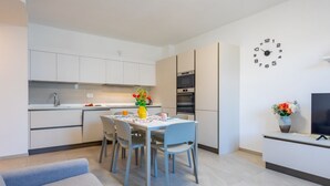 A modern kitchen with white cabinets, a dining table with chairs, a clock on the wall, and a TV on a stand. - WANT OF LAKE by Design Studio (Colico)