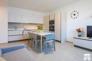 Eine moderne Küche mit weißen Schränken, einem Esstisch mit Stühlen, einer Wanduhr und einem Fernseher auf einem Schrank.