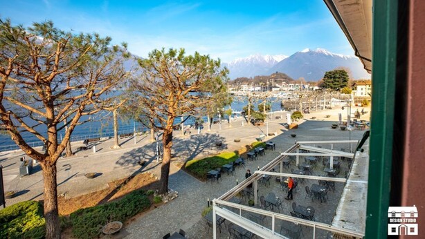 A terrace with outdoor seating overlooking a coastal town and mountains. - WANT OF LAKE by Design Studio (Colico)