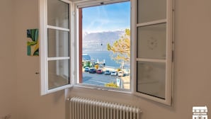 A room with a large window offering a view of a body of water and mountains. - WANT OF LAKE by Design Studio (Colico)