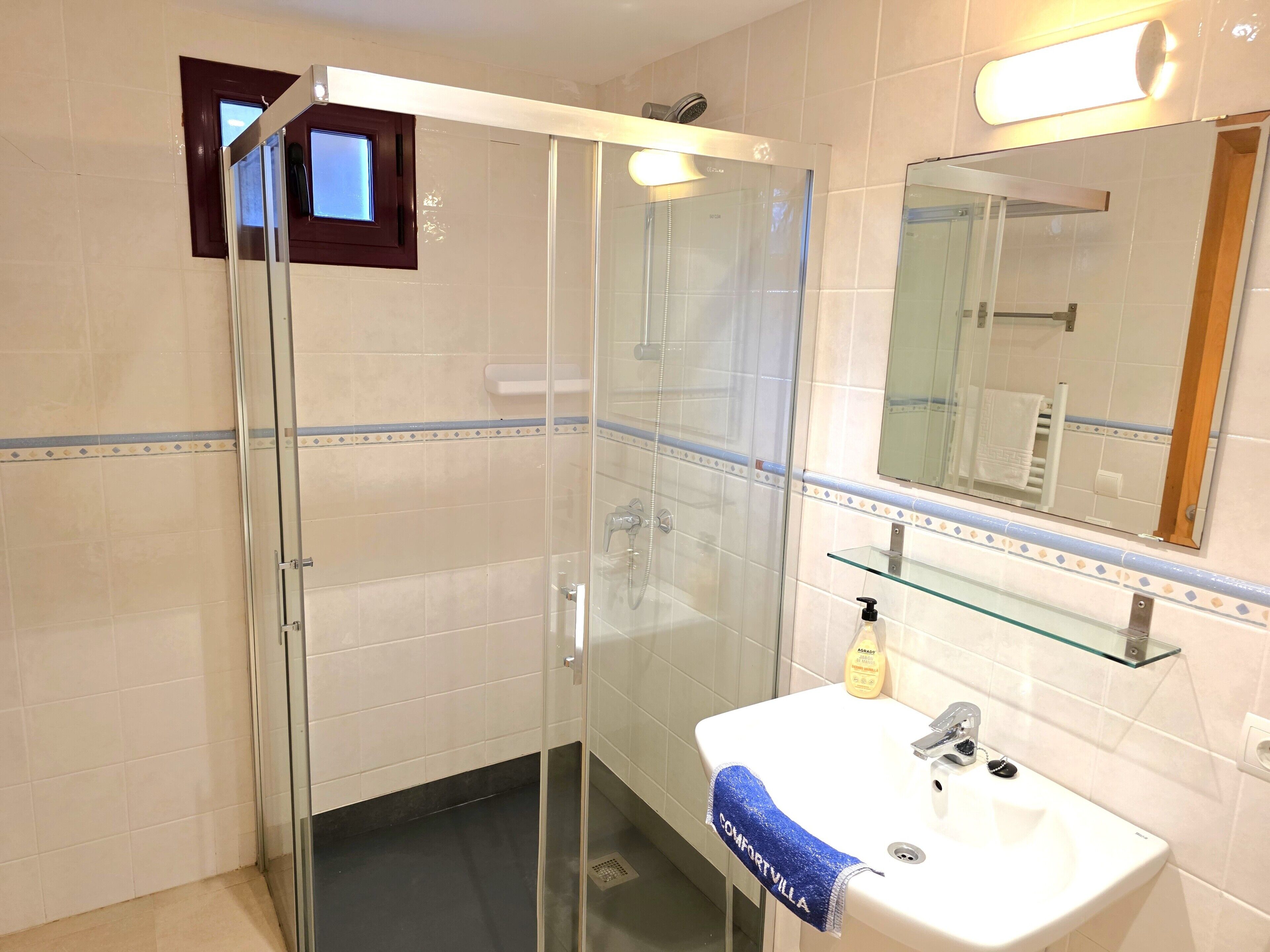 Une salle de bain moderne avec une douche à parois de verre, un lavabo blanc doté d’un distributeur de savon et un miroir au-dessus du lavabo.