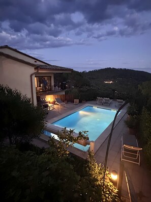 Une piscine entourée de chaises longues et de verdure, ainsi qu’un bâtiment doté d’un balcon.