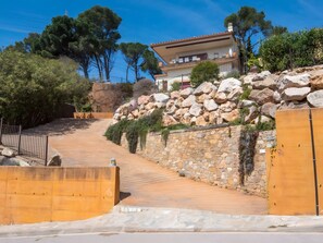 Un mur de pedra amb una porta de fusta, un camí empedrat i un edifici amb un balcó.
