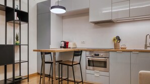 Moderni keittiö, jossa on puinen pöytä, kaksi tuolia, sisäänrakennettu uuni ja riippuvalaisin.