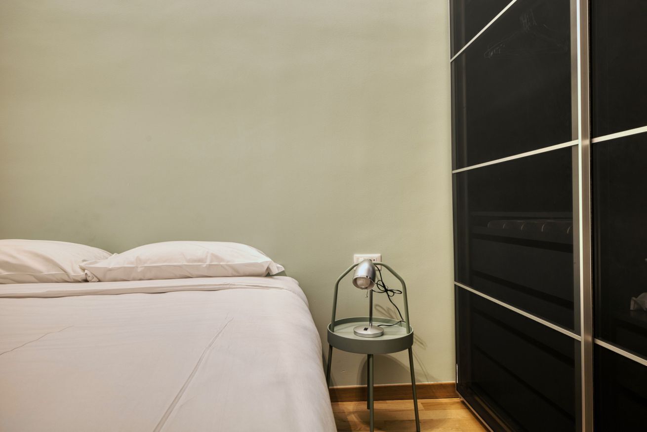 A bed with white bedding, a small table with a lamp, and a black wardrobe.