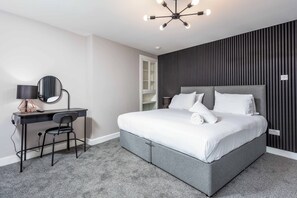 Quarto moderno com cama cinza, escrivaninha com cadeira, espelho redondo e luminária no teto.
