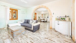 Un salon comprenant un canapé, une table basse, un coin repas avec une table et des chaises, et un coin cuisine avec des placards et un plan de travail.