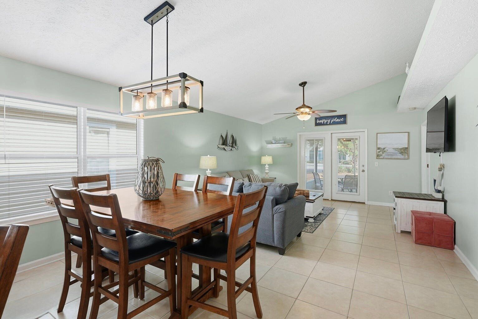 A dining area with a wooden table and chairs, a hanging light fixture, and a ceiling fan.