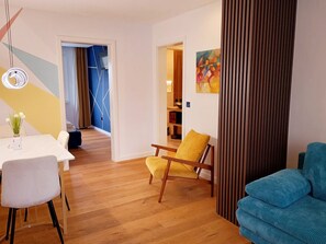 Ein modernes Wohnzimmer mit Essbereich, Holzboden, einem gelben Sessel, einem blauen Sofa und einem Bild an der Wand.