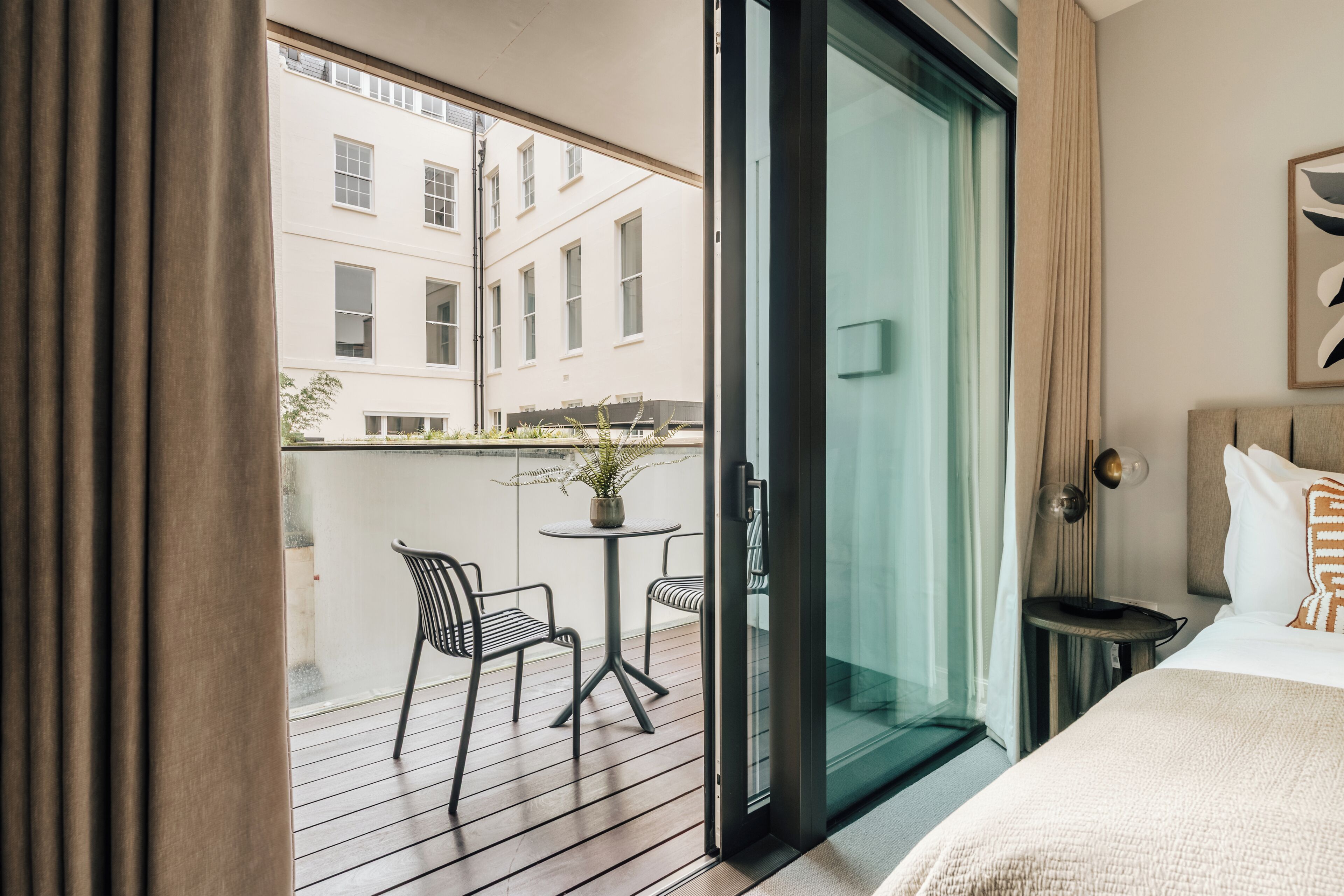 A hotel room with a balcony, a bed, a small table with chairs, and a potted plant.