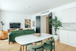 Un salon moderne avec un canapé vert, une table à manger avec des chaises, un téléviseur et une plante en pot.