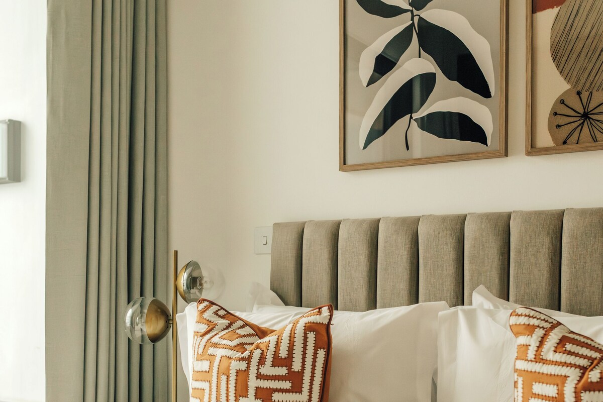 A neatly made bed with patterned pillows, a headboard, and framed artwork on the wall.