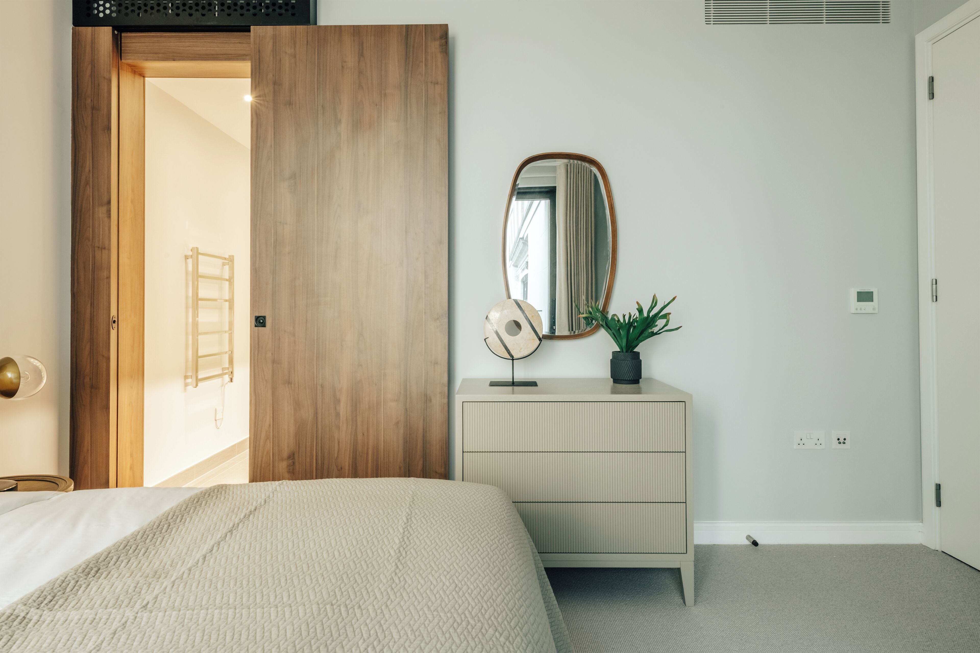 Quarto com cama, guarda-roupa de madeira, penteadeira com espelho e um vaso de planta.