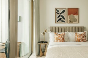 Une chambre d’hôtel avec un lit, une table de chevet, une lampe et deux œuvres d’art encadrées accrochées au mur.