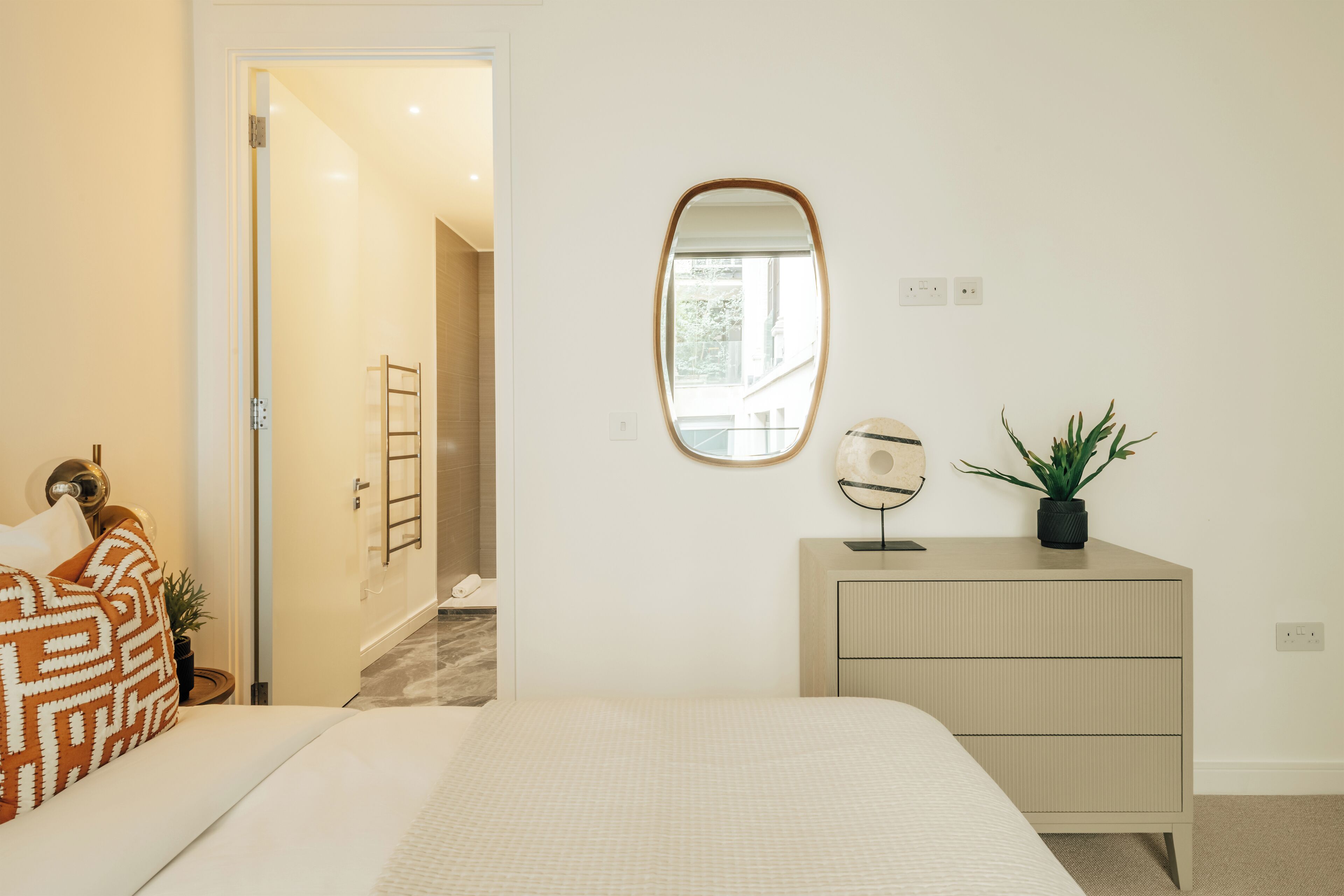 Un dormitorio con una cama, un aparador, un espejo y una planta en maceta.