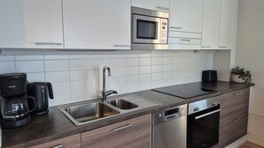 A modern kitchen with white cabinets, a Bosch microwave, a sink, a coffee maker, and a dishwasher. - M&J Apartments Harbour (Jyväskylä)