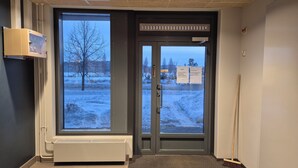 A hotel entrance with a glass door, a radiator, and a broom leaning against the wall. - M&J Apartments Harbour (Jyväskylä)