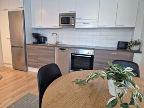 A modern kitchen with white cabinets, stainless steel appliances, and a wooden dining table with chairs. - M&J Apartments Harbor   (Jyväskylä)