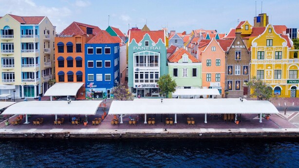 A row of colorful buildings along a waterfront, with outdoor seating areas and a canal in the foreground. - The Wharf 5A in Willemstad (Willemstad)