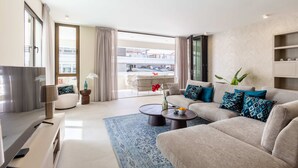 A modern living room with a sofa, coffee table, and TV. There is a balcony with a view of a building. - The Wharf 5A in Willemstad (Willemstad)
