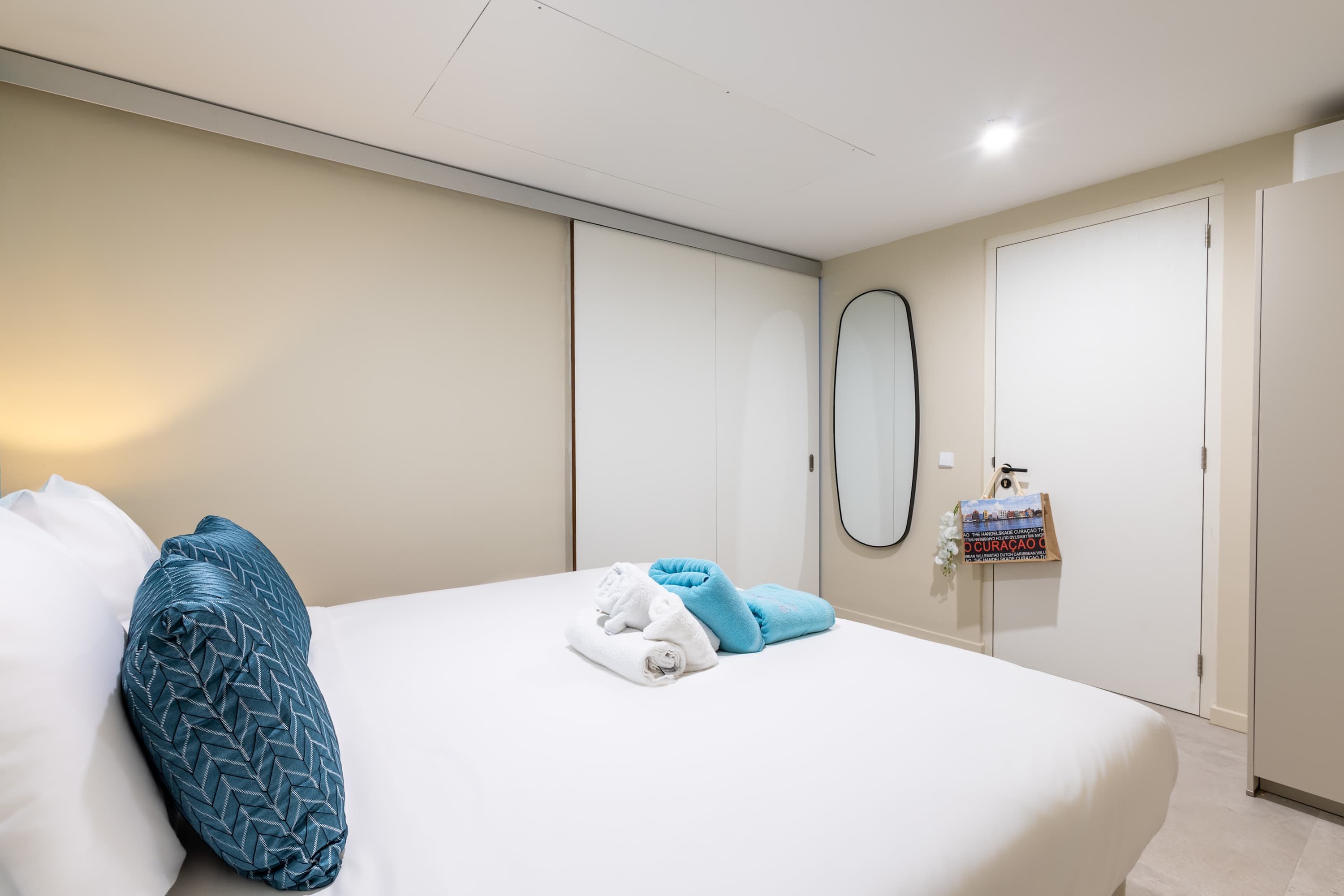 A neatly made bed with a blue and white pillow, a folded towel, and a small decorative item on the nightstand.