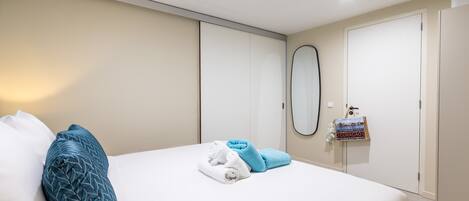 A neatly made bed with a blue and white pillow, a folded towel, and a small decorative item on the nightstand.