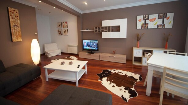 Un salon moderne doté d’un téléviseur à écran plat, d’un canapé, d’une table basse, d’une table à manger et d’un tapis en peau de vache.