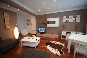 Un salon moderne doté d’un téléviseur à écran plat, d’un canapé, d’une table basse, d’une table à manger et d’un tapis en peau de vache.