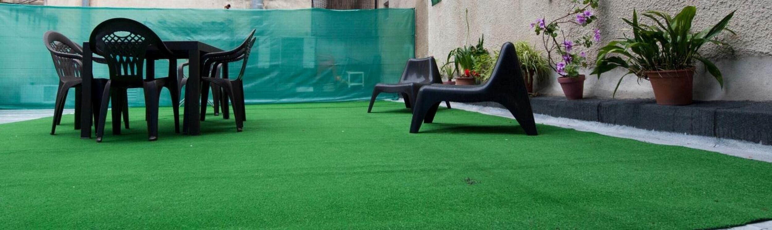 Un espacio al aire libre con césped artificial, sillas de plástico y plantas en macetas.