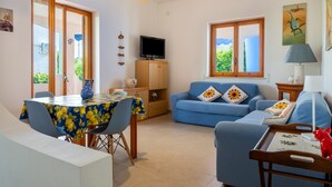 Ein Wohnzimmer mit einem blauen Sofa, einem Esstisch mit Stühlen, einem Fernseher und einer Lampe.