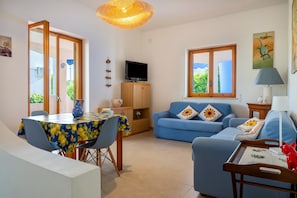 A living room with a blue sofa, a dining table with chairs, a TV, and a lamp. - Villa 'Ingrosso' with Sea View, Wi-Fi and Air Conditioning (Leporano Marina)