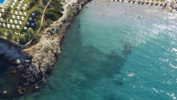 Eine Luftaufnahme eines Küstenresorts mit Schwimmbad, Strandstühlen und einer felsigen Küstenlinie.
