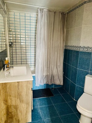Une salle de bain avec un lavabo blanc, une douche avec un rideau à rayures et des murs recouverts de carreaux bleus.