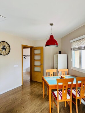 A dining area with a wooden table and chairs, a red pendant light, a whiteboard, and a clock on the wall.