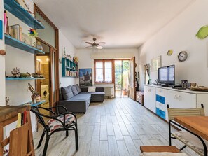 Ein gemütliches Wohnzimmer mit Sofa, Esstisch und Fernseher. Regale mit Büchern und Dekoration, und ein Fenster mit Aussicht.