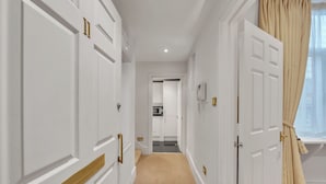 Un passadís amb portes blanques, una catifes beix i una finestra amb cortines beix.