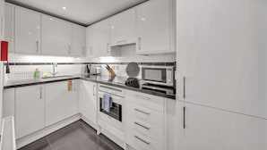 Una cuina moderna amb armaris blancs, tauleig negre, microones, torradora i un rentaplat.